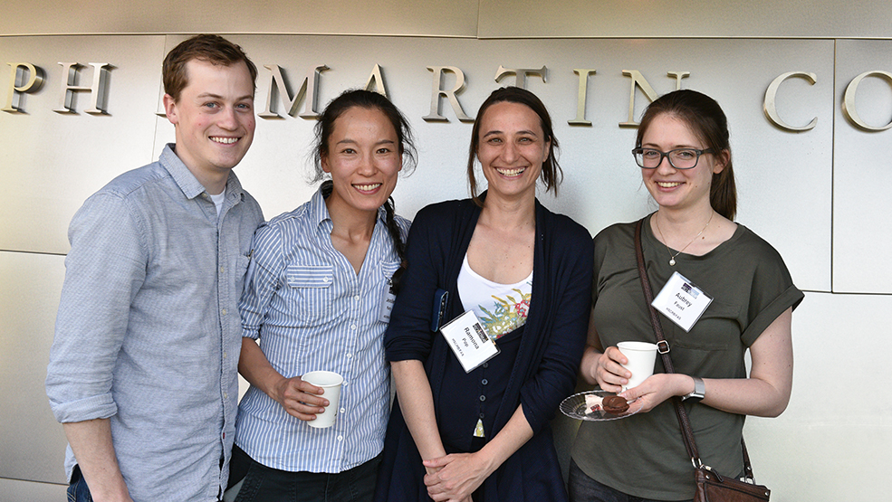 Three scientists smiling in front of a titanium-clad wall