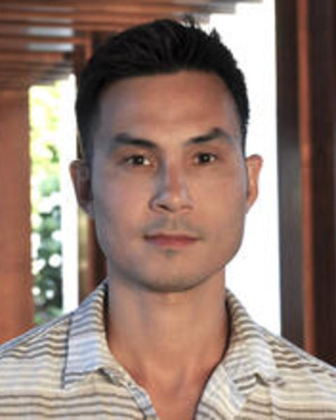 Man with short dark hair wearing a white and brown striped polo
