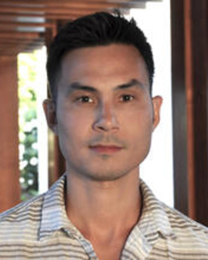 Man with short dark hair wearing a white and brown striped polo